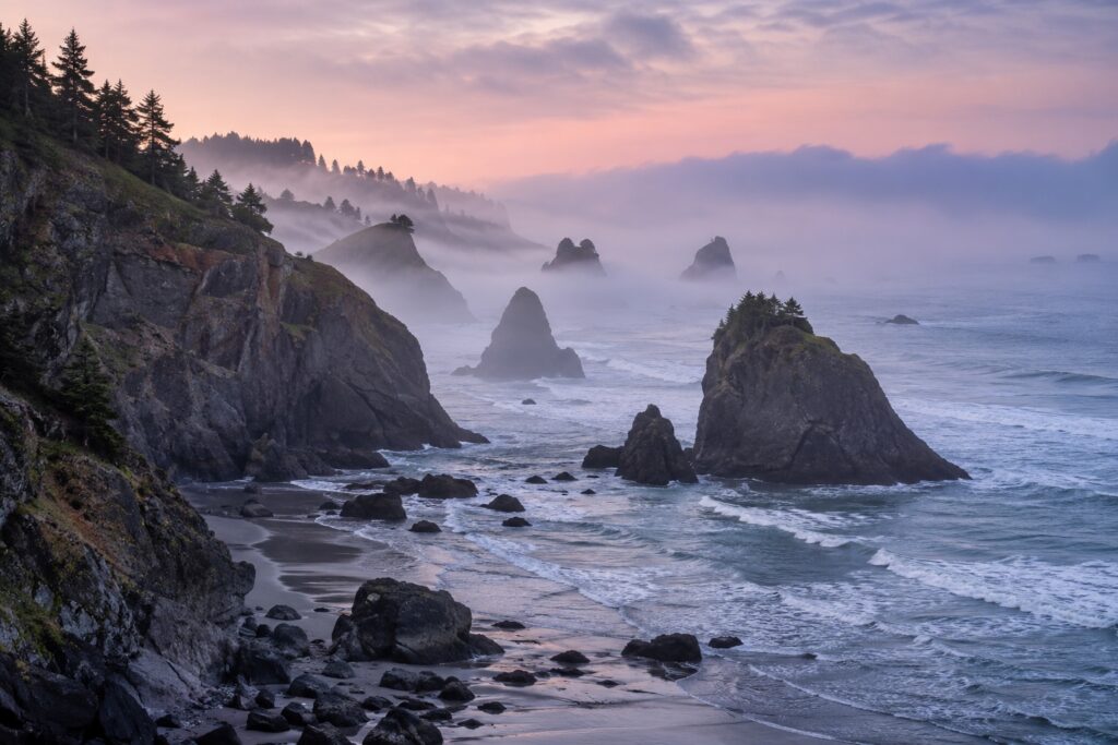 Misty coastal cliffs and sea stacks beneath a pink morning sky