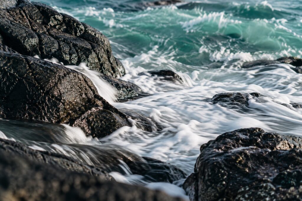Sea foam washing around dark coastal basalt stones